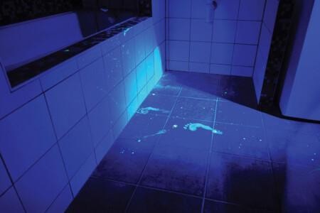 UV-valolla valaistu kylpyhuone, jossa näkyy UV-valossa loistavia jalanjälkiä